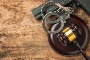 Handcuffs, gun, and gavel on wood; Lori Beck Law Office handles firearm and weapons charges in Denver, CO.