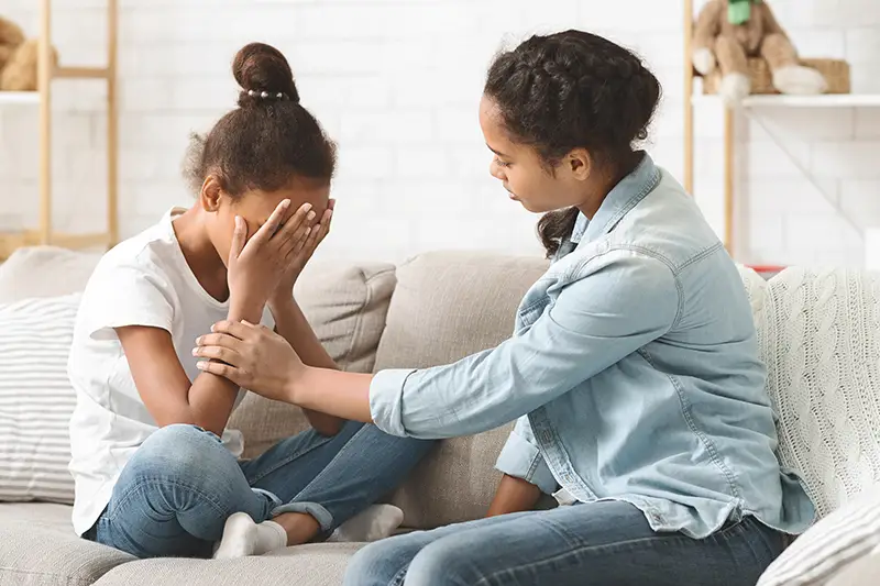 Older sister comforting crying younger sister; Lori Beck Law Office offers family support for juvenile criminal defense in Denver, CO.