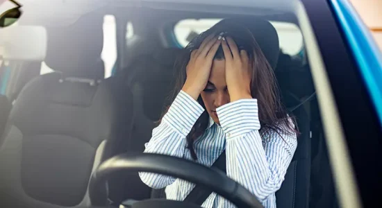 Woman with hands on head in distress inside a car, symbolizing accident stress