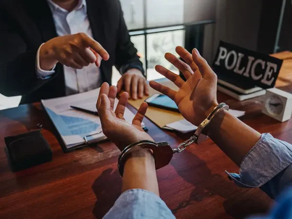 Handcuffed person with police in an interrogation room; Lori Beck Law Office offers defense against false arrests in Denver, CO.